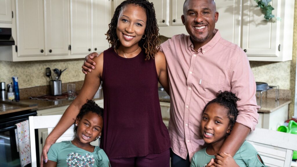 Scott Colom smiles with his wife and two daughters in their Columbus kitchen