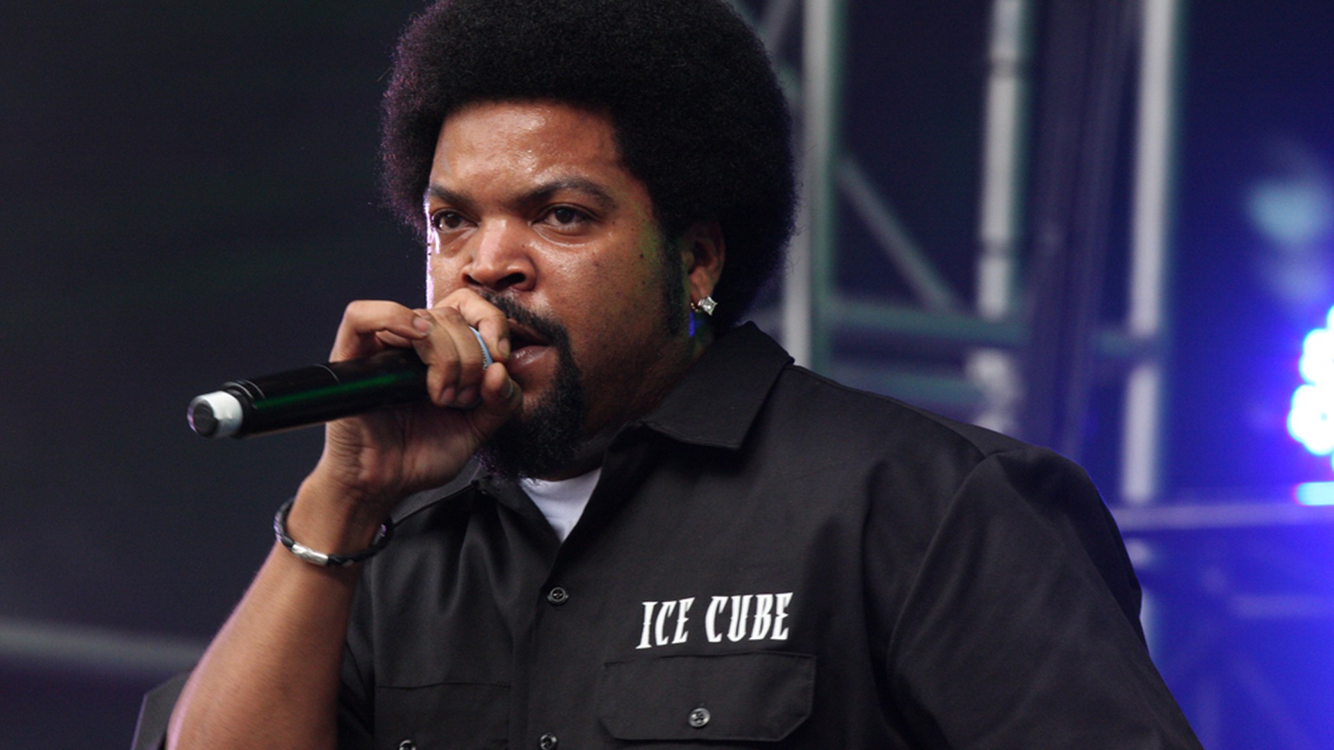 Ice Cube performs on stage holding a microphone in a black shirt