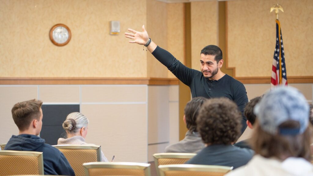 Abdul El Sayed speaking to voters at a campaign meeting with his hand raised