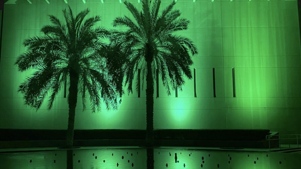 The United States Embassy in Riyadh Saudi Arabia lit green at night behind palm trees