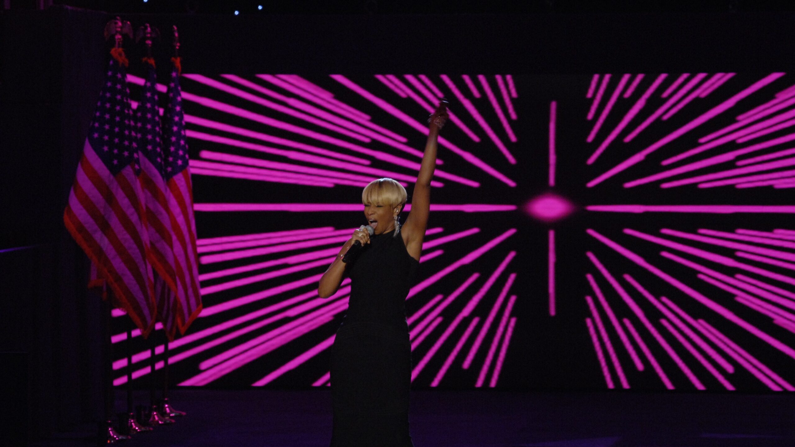 Mary J. Blige performs on stage in a black dress with one arm raised