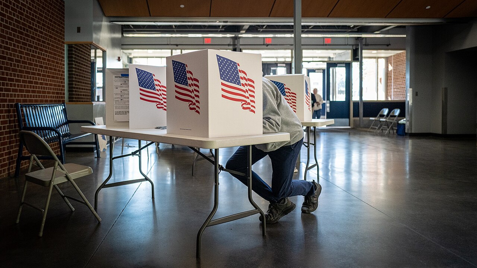 A voter casting a ballot at a polling place with flag marked booths