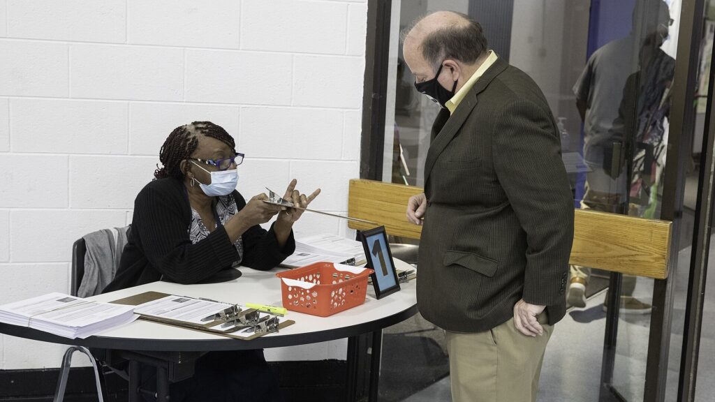 A Black poll worker seated at a table helping a voter at a Detroit polling site