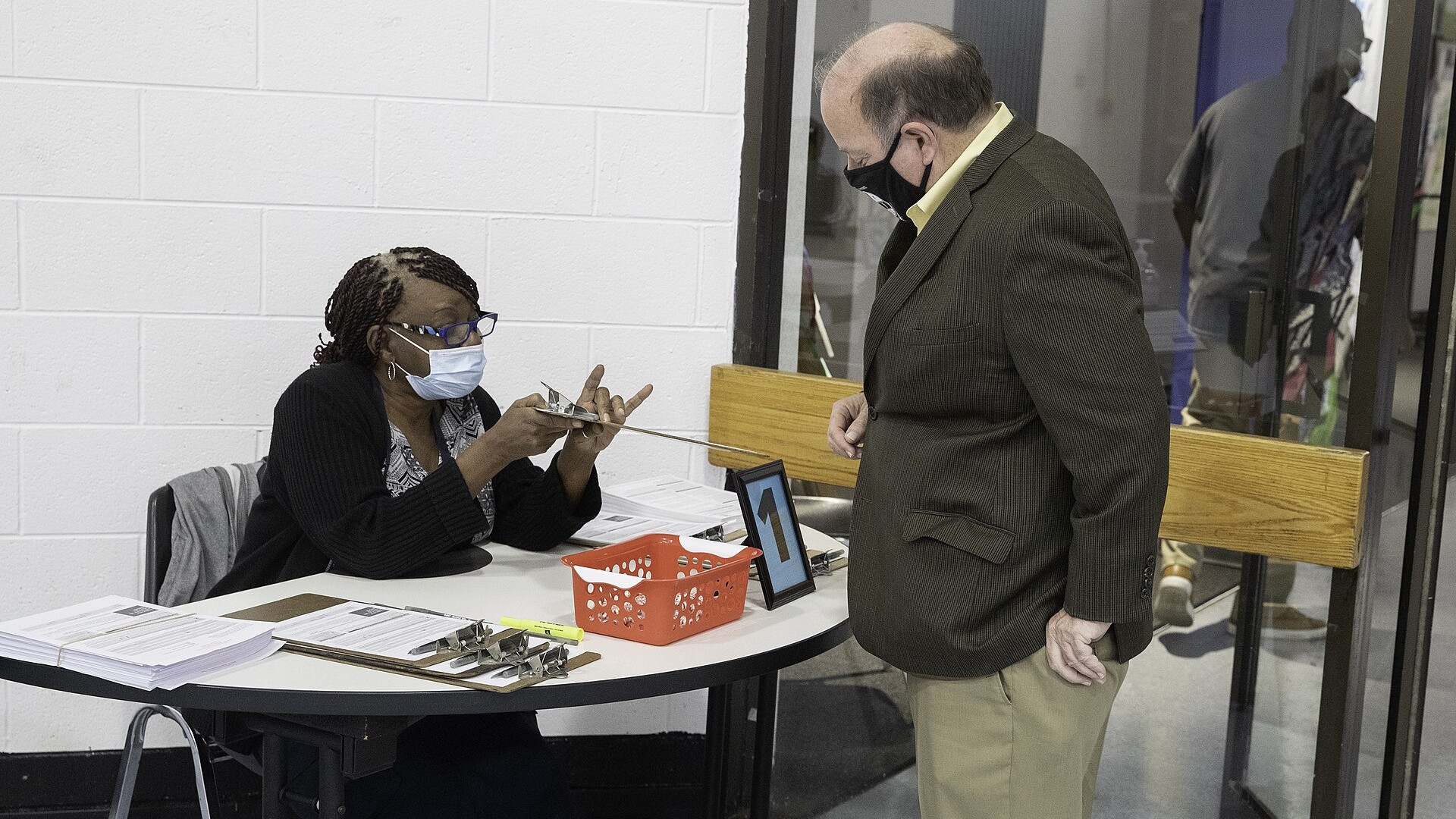A Black poll worker seated at a table helping a voter at a Detroit polling site