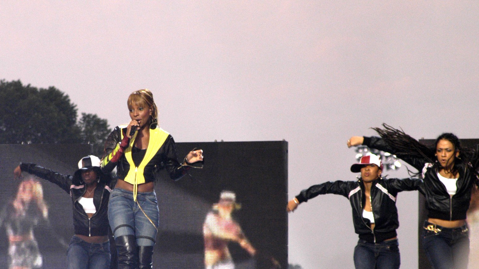 Mary J. Blige sings on an outdoor stage with dancers beside her