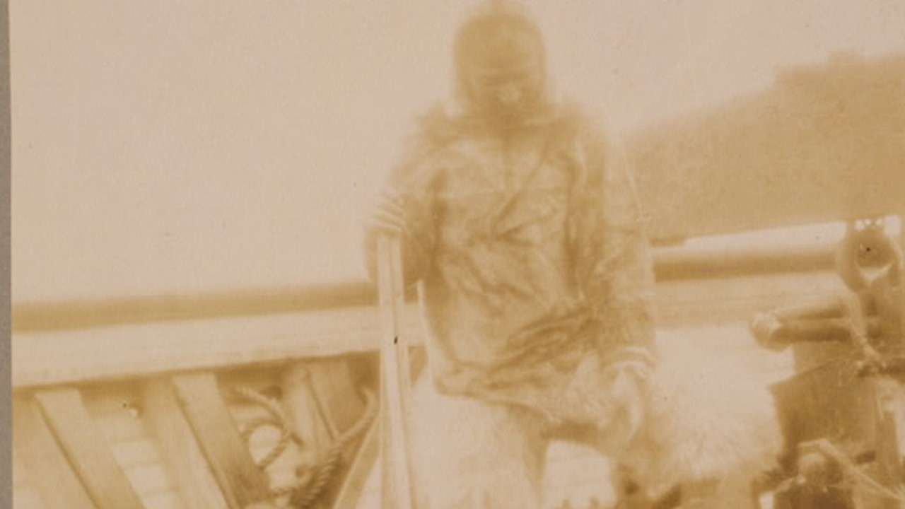 Matthew Henson in Arctic dress standing on the deck of the Roosevelt with a sled dog