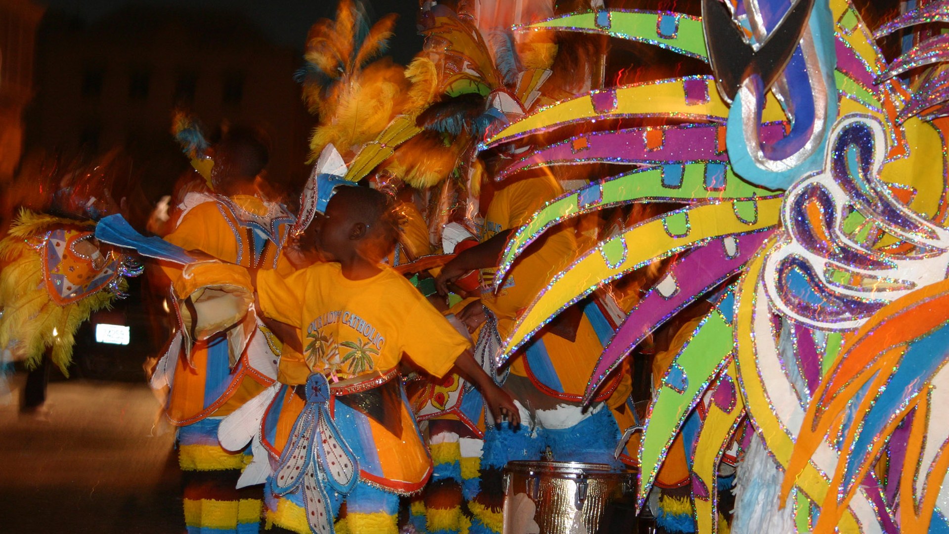 Junkanoo performers in bright feathered costumes dancing at night in Nassau