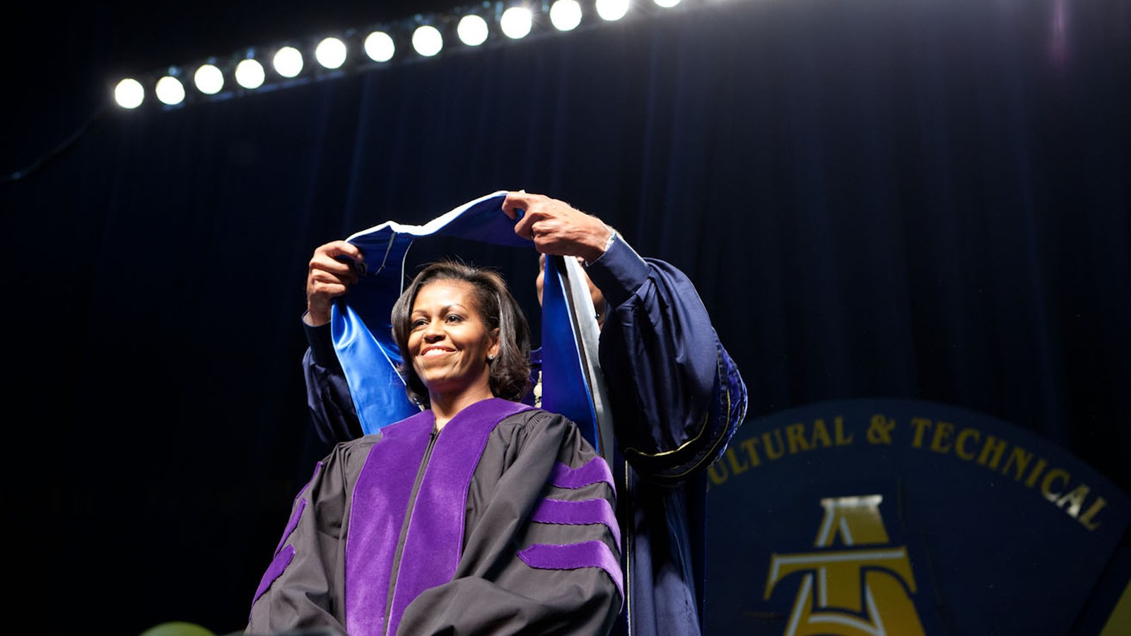 Michelle Obama smiling as she receives an academic hood during commencement at the university in Greensboro in 2012
