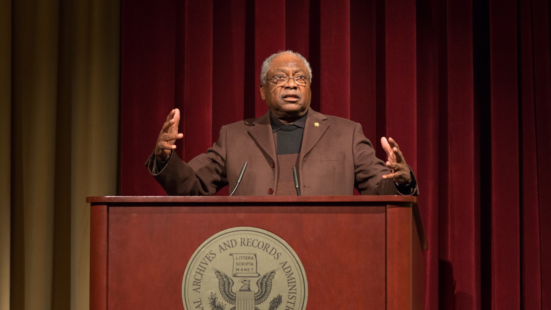 Representative Jim Clyburn speaking at a podium with hands raised
