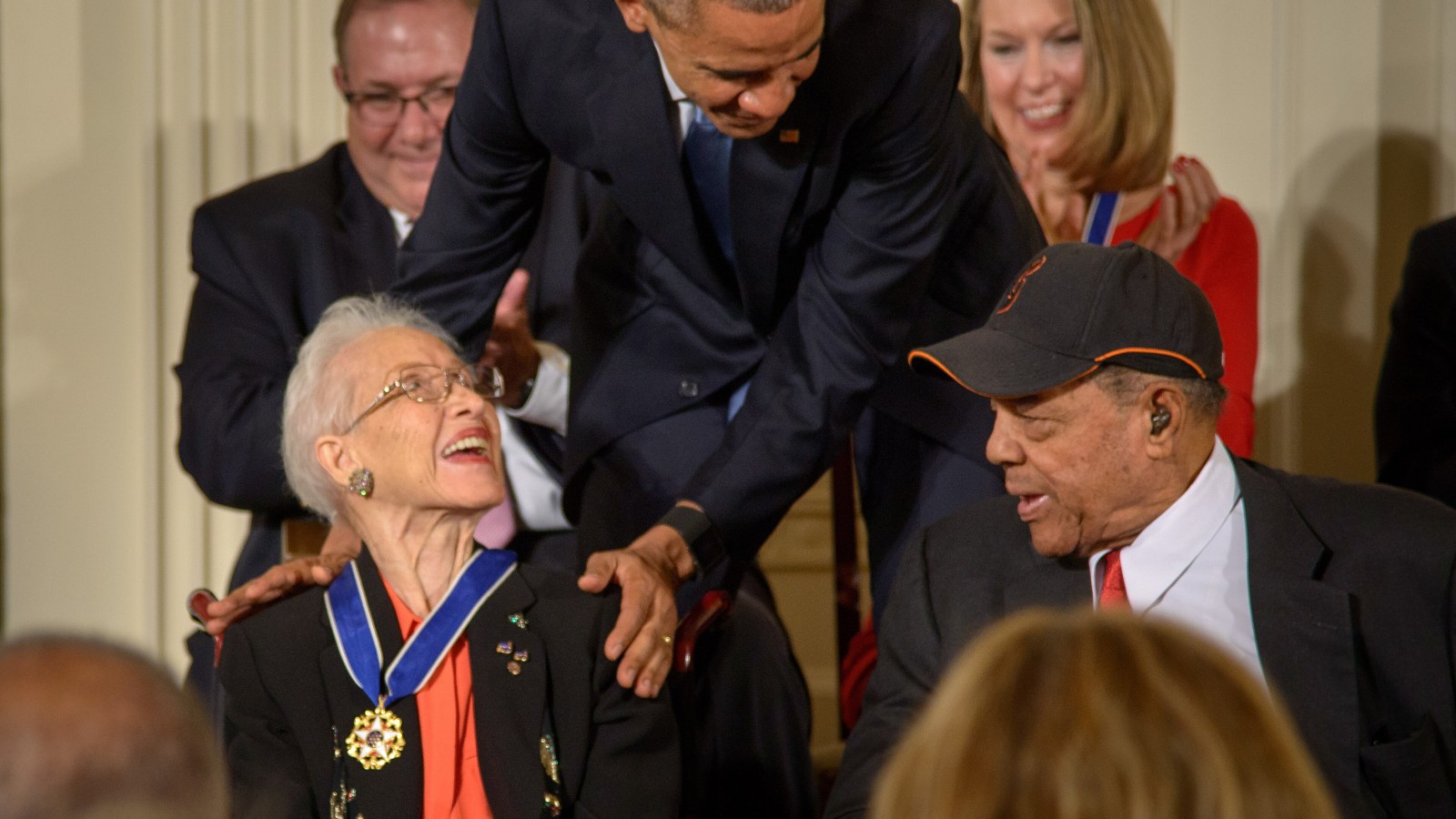 Katherine Johnson wearing the Presidential Medal of Freedom and laughing as President Barack Obama leans down to speak with her in 2015