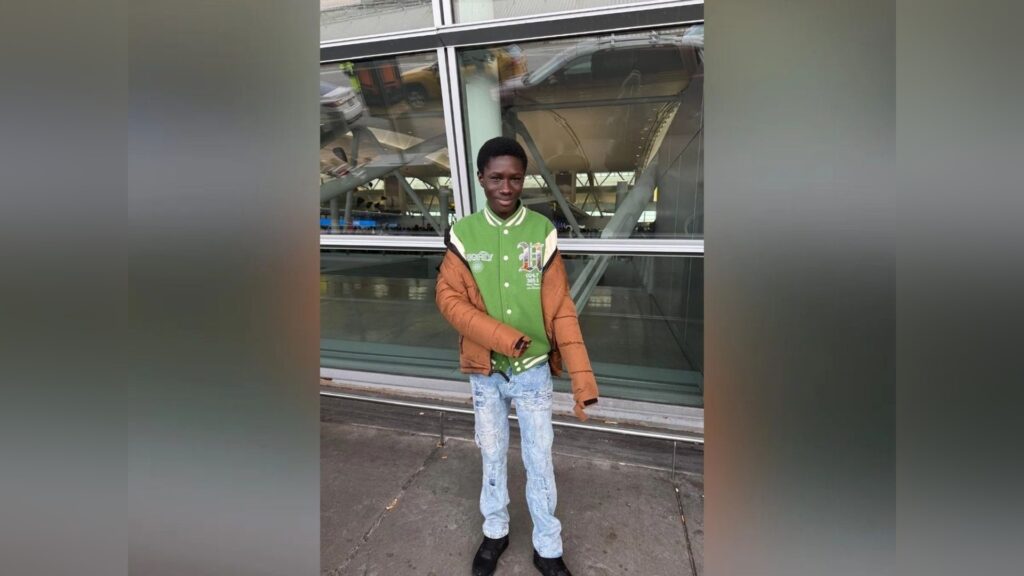 Javits Frimpong standing outside in a green varsity jacket and jeans