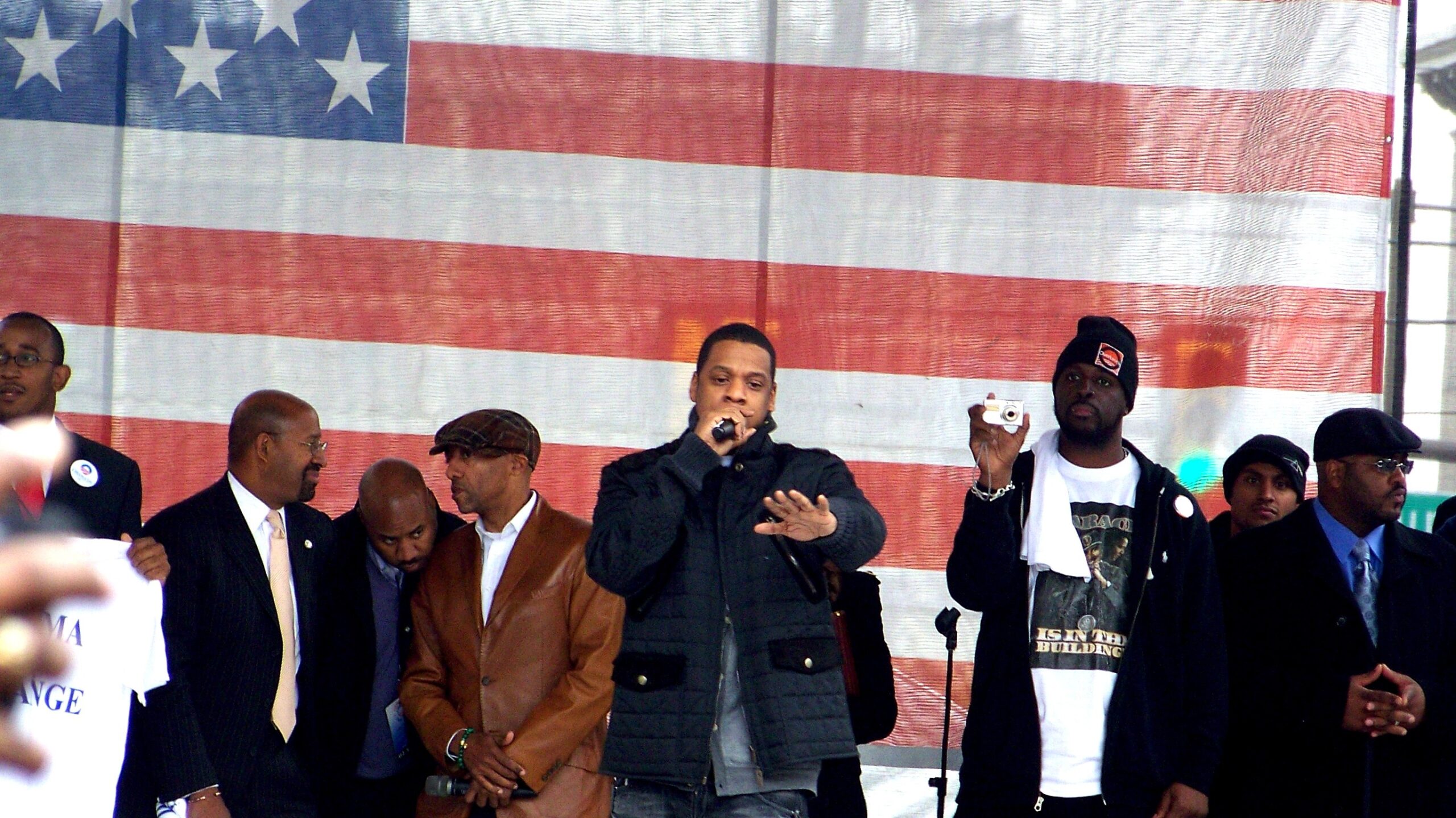 Jay-Z speaks into a microphone in front of a giant American flag