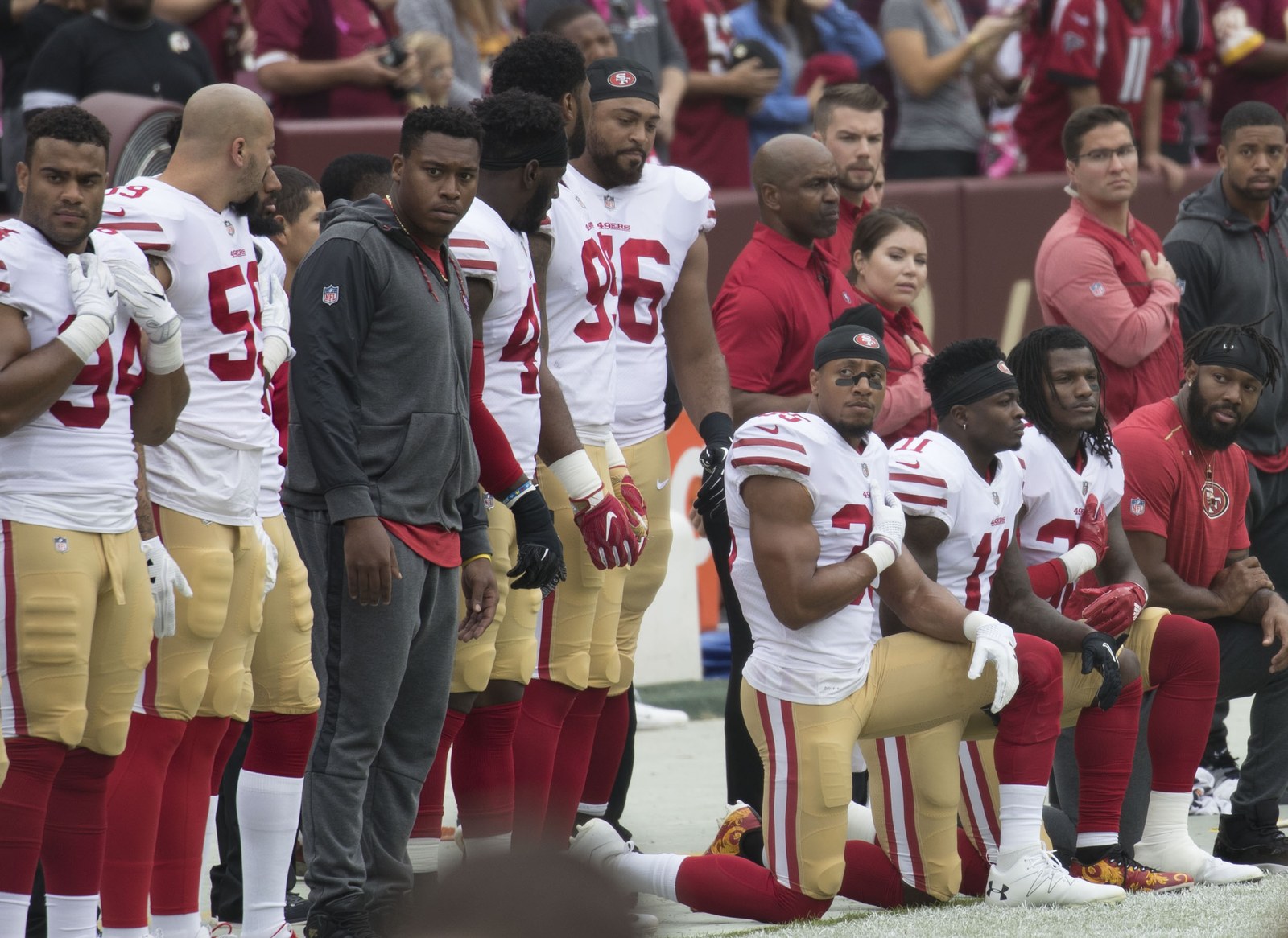San Francisco 49ers players kneel during the national anthem while teammates stand beside them