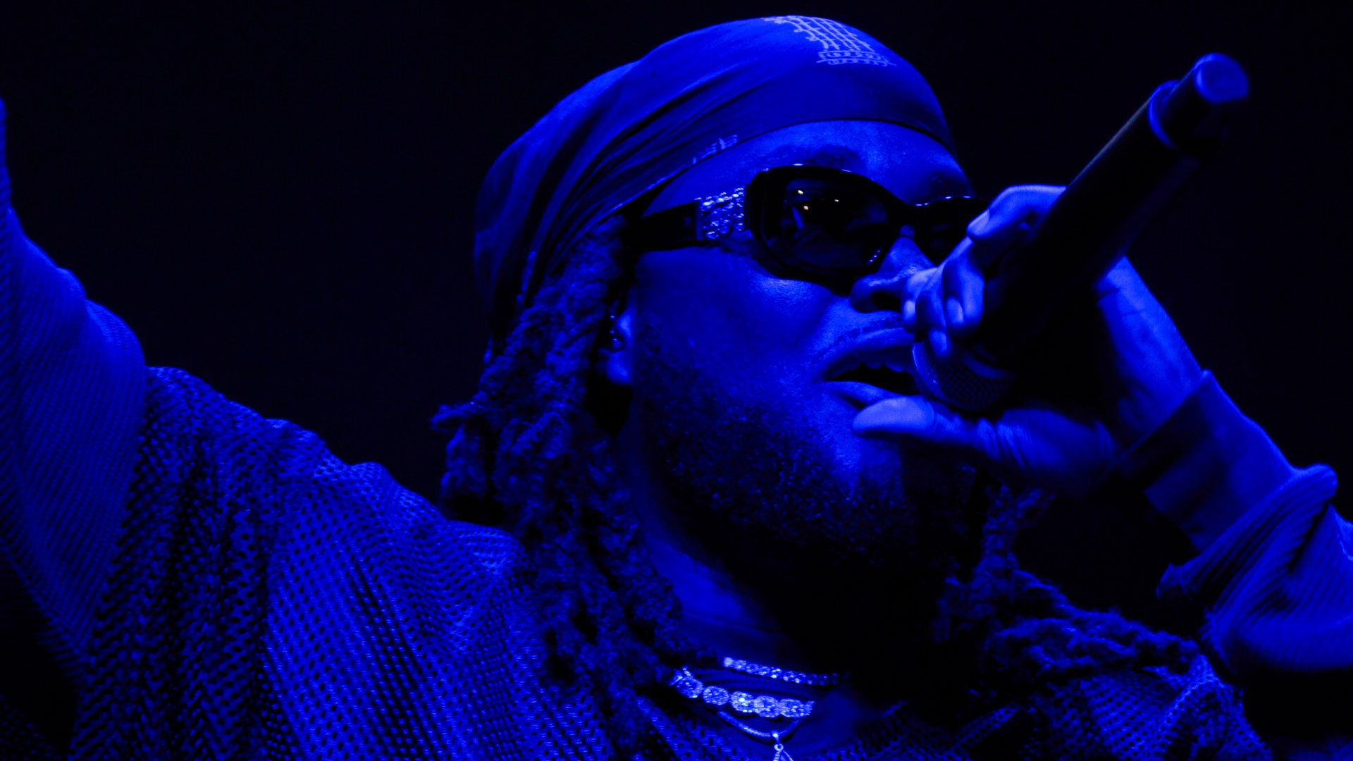 Leon Thomas performs on stage in blue light holding a microphone