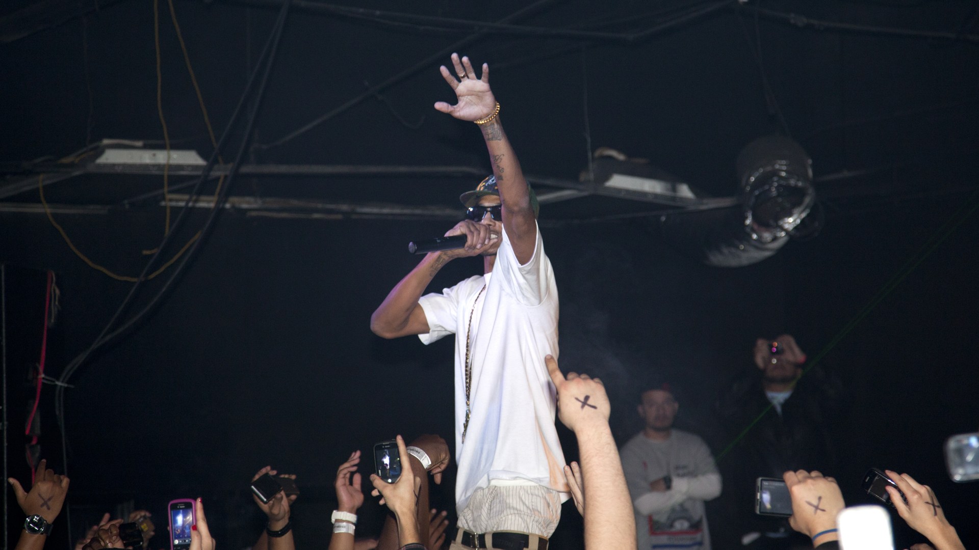 Nipsey Hussle performing on stage with a microphone in hand and one arm raised toward the crowd