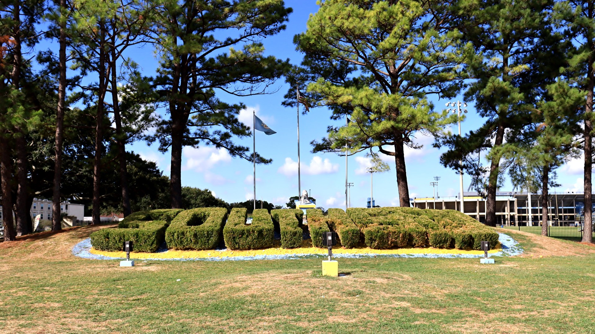 The word Southern spelled out in trimmed hedges on a grassy hill on the Southern University campus in Baton Rouge, with pine trees, flags and the stadium behind it
