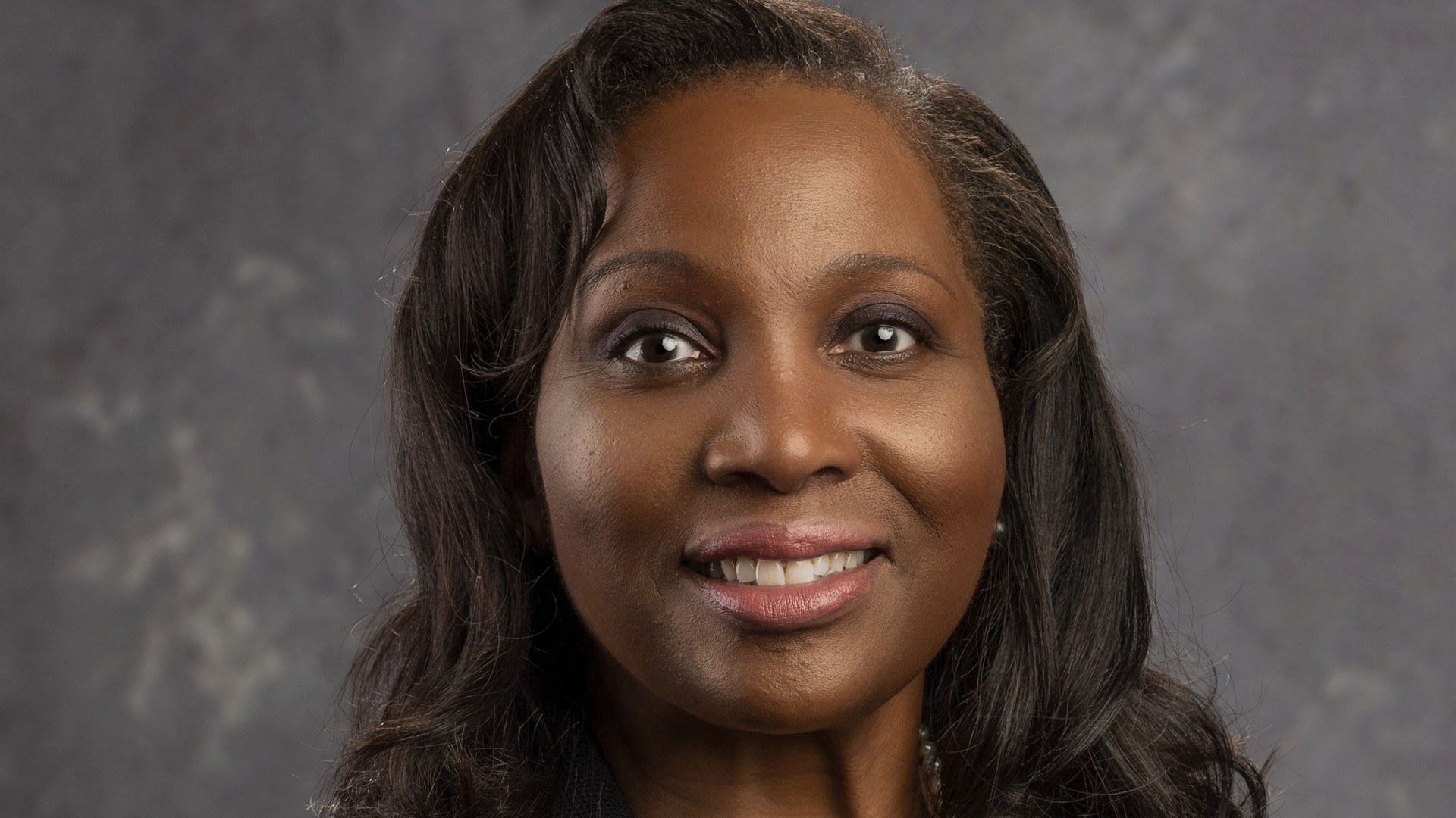 Official portrait of Federal Reserve Governor Lisa Cook smiling against a gray backdrop