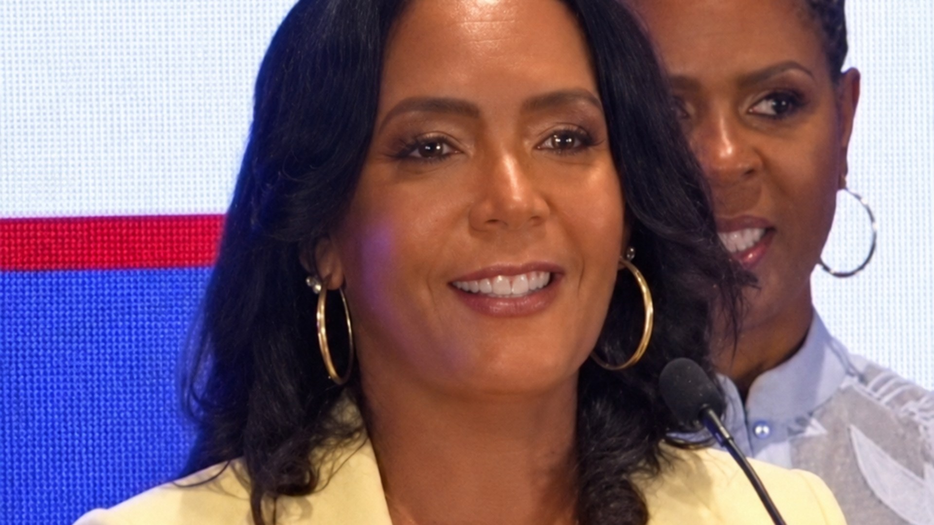 Keisha Lance Bottoms smiling at a podium in a yellow blazer